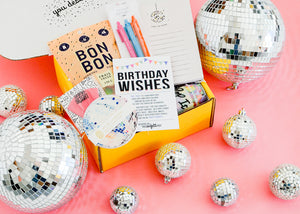 Birthday gift box show open with gifts inside. On pink bacckdrop surrounded by disco balls