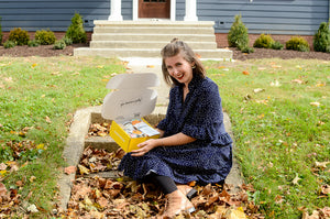 Young women holding aYoung women holding an open gift box on a doorstep with a smile on her facen open gift box on a doorstep with a smile on her face