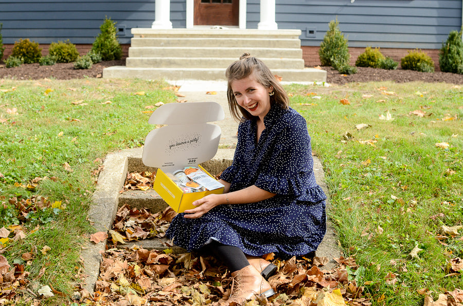 Young women holding an open gift box on a doorstep with a smile on her face