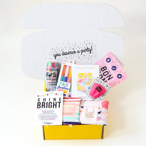 Open Graduation gift box with assorted color pens, candy, proud of you sticker, shine bright card, confetti