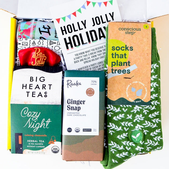 Eco-friendly Giving Green Gift Box for Her employees and friends. Filled with sustainable and earth friendly gifts for the holidays: Green Brancches Socks, Ginger Snap Candy Bar, Cozy Nights Herbal Tea, Holly Jolly Greeting Card, Be Jolly Balloon, and Confetti Popper