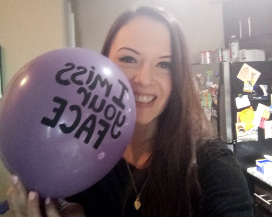 Woman smiling and taking a selfie with a purple balloon by her face with the words 