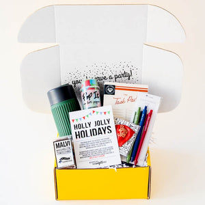 Open gift box filled with greeting card pens, task pad, confetti and drink cup in blue, greens and reds